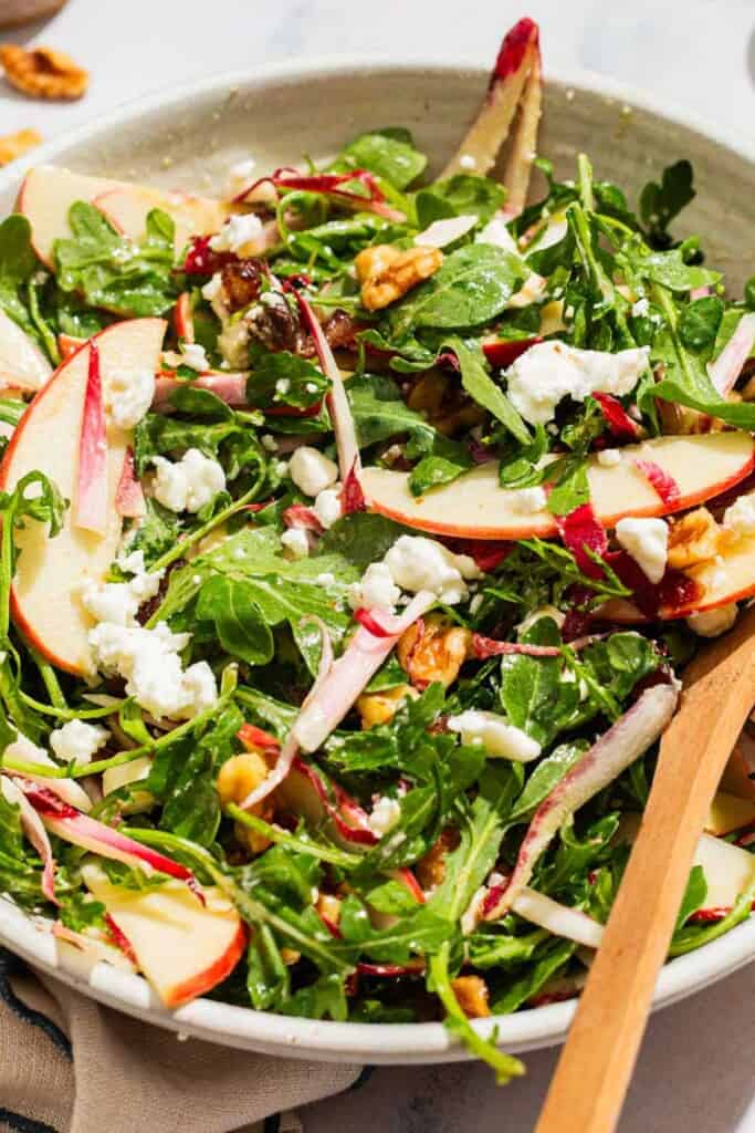 Apple walnut salad in a serving bowl with wooden serving utensils.