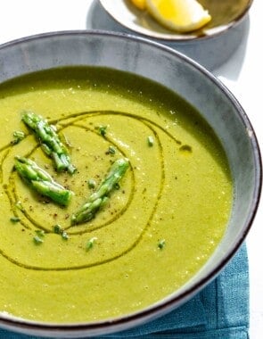 A close up of a bowl of asparagus soup. Next to this is a small plate of lemon wedges.