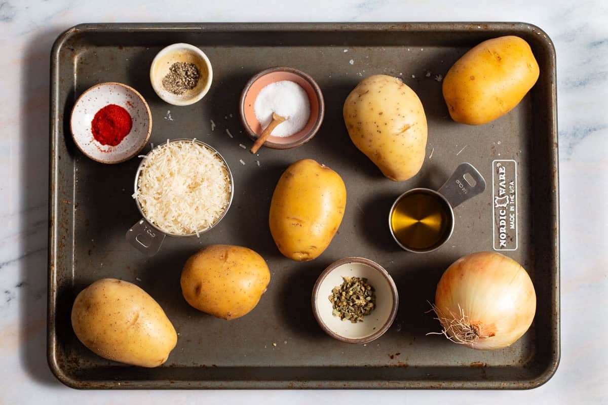 Ingredients for baked hash browns including yukon gold potatoes, onion, grated parmesan, oregano, paprika, salt, pepper, and olive oil.