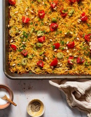 Baked hash browns on a sheet pan next to a kitchen towel and bowls of salt and pepper.