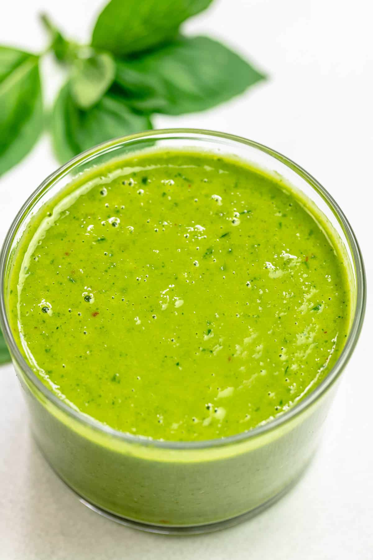 basil vinaigrette in a small jar with basil leaves in the background.