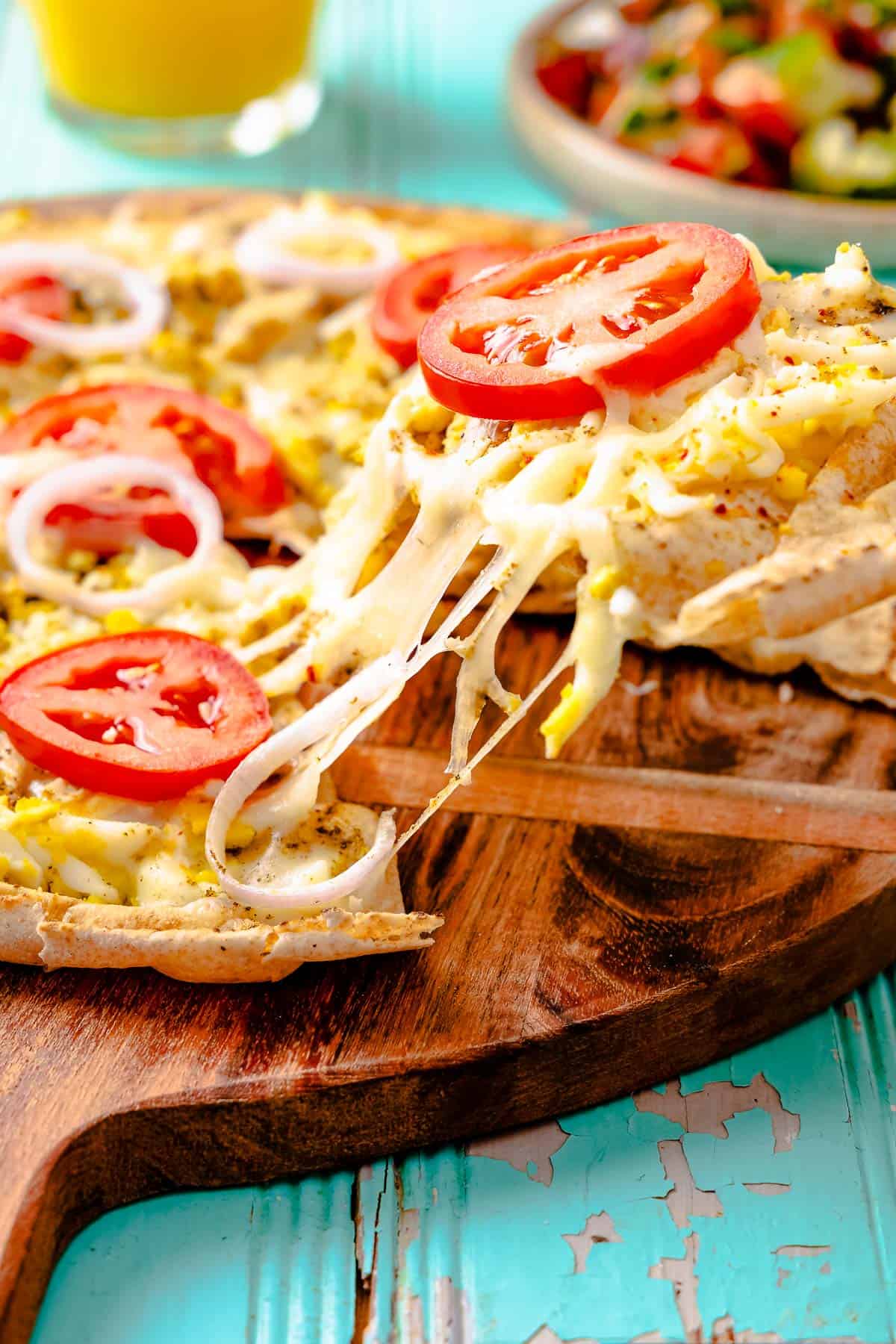 a slice of pita breakfast pizza being lifted away from an entire breakfast pizza on a wooden serving platter.