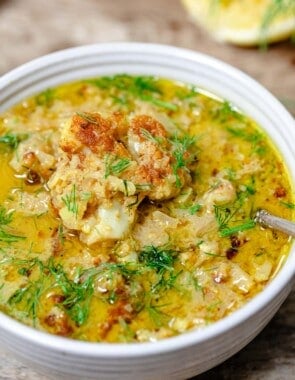 a close up of roasted cauliflower soup in a bowl with a spoon garnished with dill.