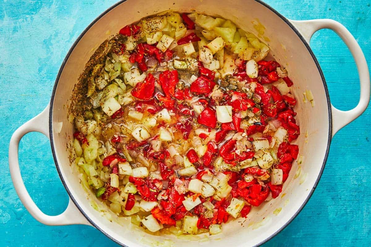 a dutch oven with cioppino ingredients including fennel, onion, roasted red peppers, oregano and thyme.