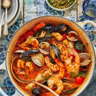 a dutch oven with cioppino ingredients including fennel, onion, roasted red peppers, oregano and thyme.