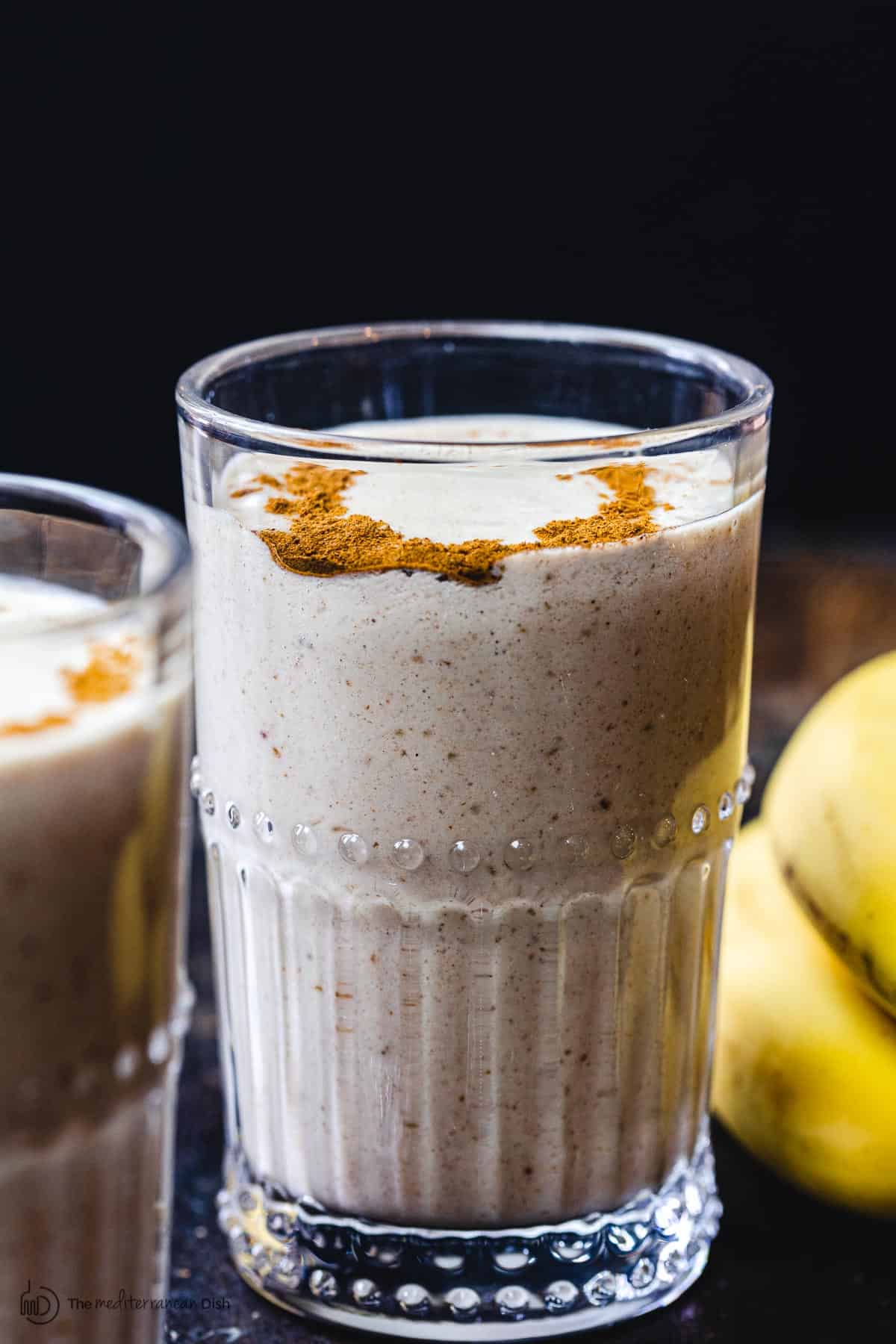 Tahini Date Banana Shake in glass. Bananas on the side