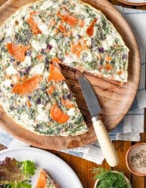 a cooked egg white frittata on a serving tray with a slice missing next to a slice of an egg white frittata on a plate with a small salad and a bowl of fresh dill.