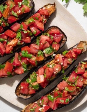 An overhead photo of 5 pieces of eggplant bruschetta on a platter next to a sprig of cilantro.