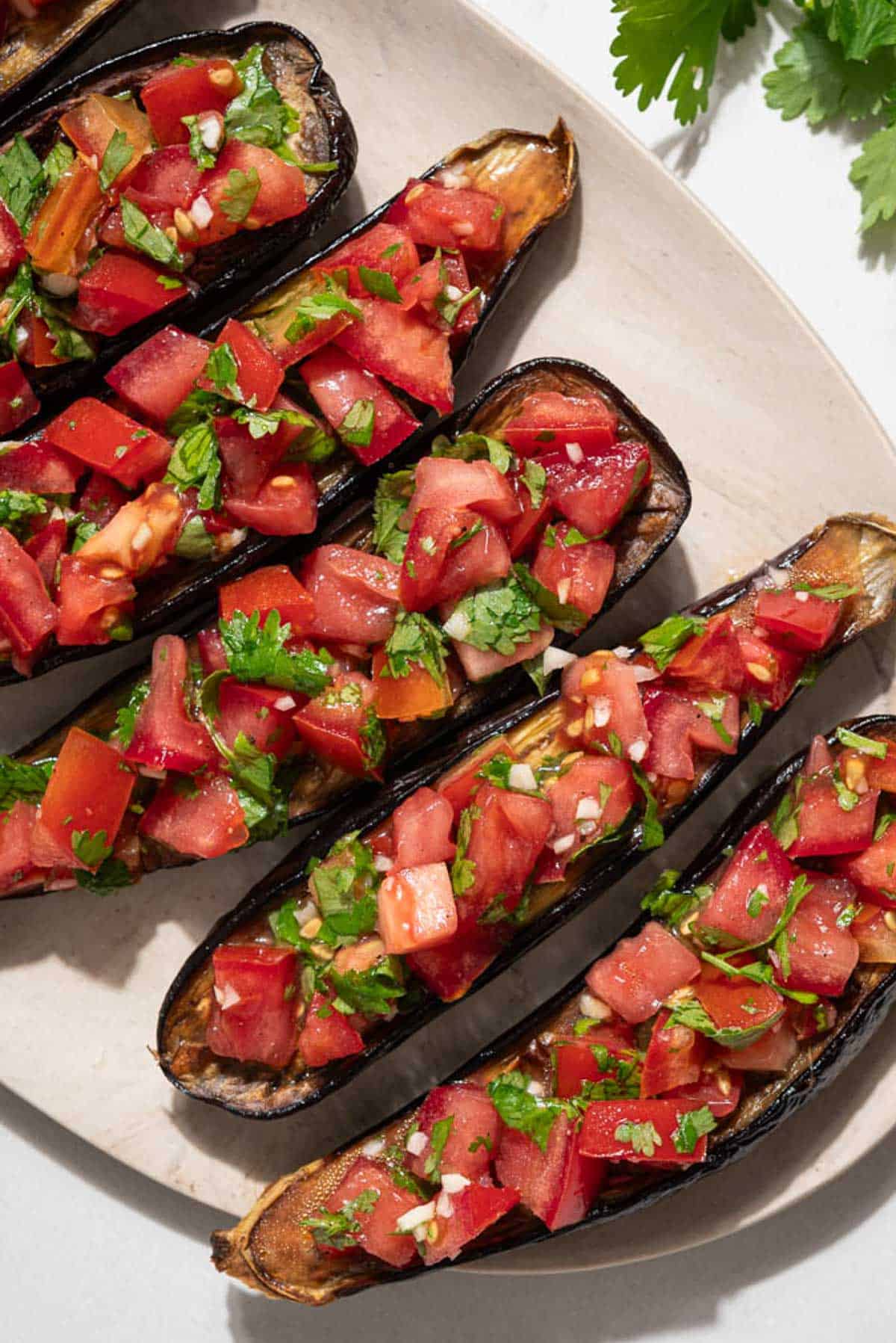 An overhead photo of 5 pieces of eggplant bruschetta on a platter next to a sprig of cilantro.