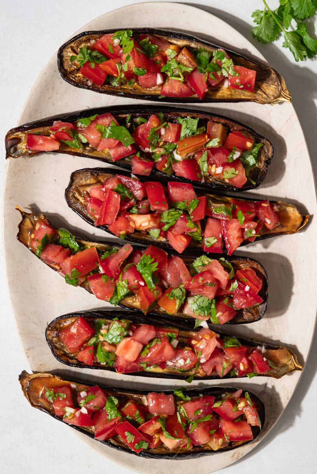 An overhead photo of 6 pieces of eggplant bruschetta on a platter next to a sprig of cilantro.