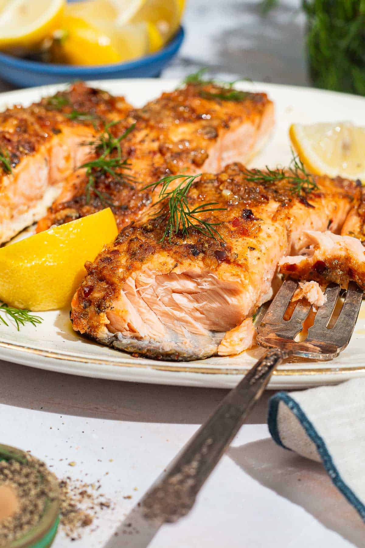 A close up photo of baked dijon salmon fillets on a serving platter with lemon wedges and a fork.