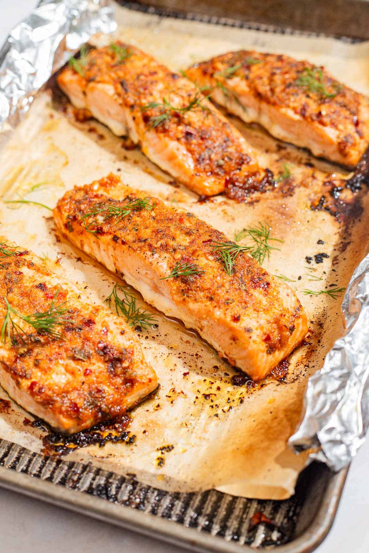 A close up of 4 baked dijon salmon fillets on a parchment and foil lined baking sheet.