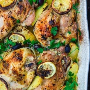 Greek chicken and potatoes garnished with parsley, olives and lemon slices