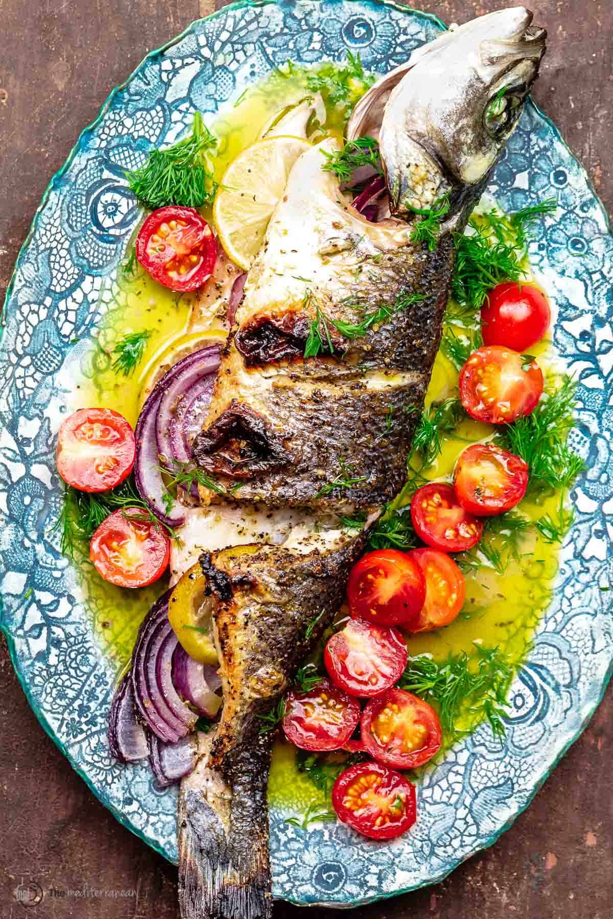 whole broiled branzino with ladolemono, cherry tomatoes, and dill on a platter