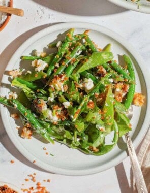 A close up of green bean and snap pea salad with crispy quinoa on a plate with a fork.