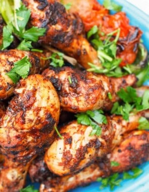 A close up of grilled chicken drumsticks garnished with parsley on a serving platter.