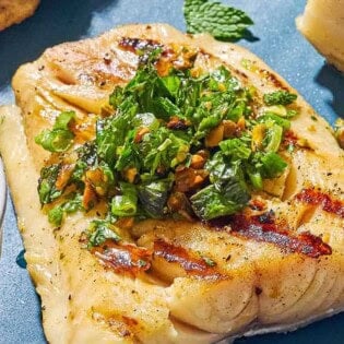 A close up of a grilled cod filet topped with pistachio-herb salsa.