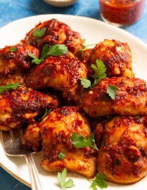 honey harissa chicken on a platter with parsley leaves on top.