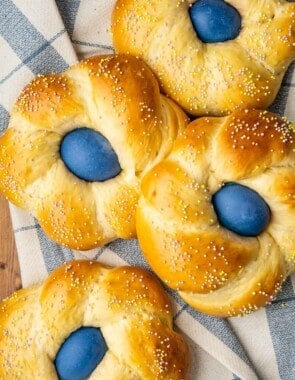 four italian easter breads each containing a blue dyed easter egg on a cloth napkin.