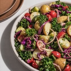 A close up of pesto potato salad in a serving bowl. Next to this is a stack of 2 plates.