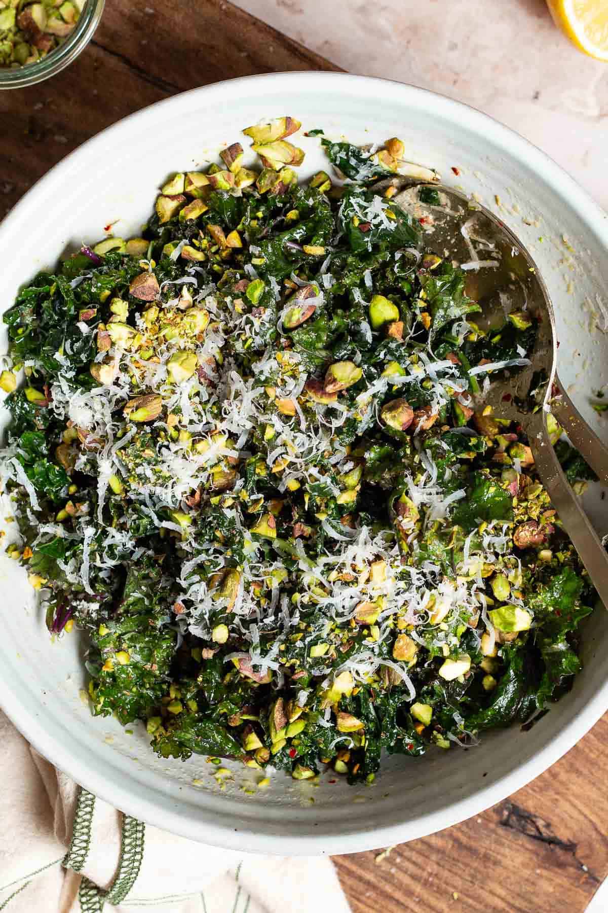 An overhead photo of kale salad in a large bowl with serving utensils on a cutting board.