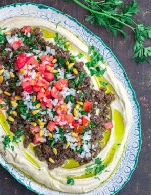 Hummus dip layered with ground beef, tomatoes, onions, parsley, and pine nuts