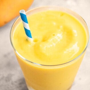 One mango smoothie in a glass with a blue straw.