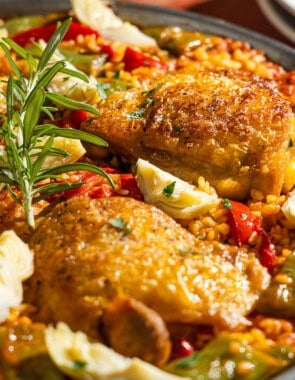 A close up of chicken paella in a large paella pan with a serving spoon.