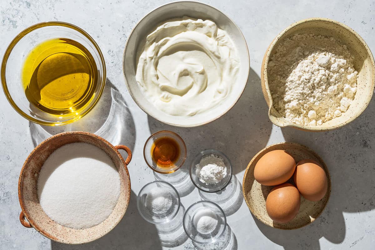 Ingredients for yogurt cake including all purpose flour, baking powder, baking soda, kosher salt, greek yogurt, granulated sugar, eggs, and vanilla extract.