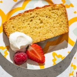 A close up of a slice of yogurt cake on a plate with a dollop of greek yogurt, a strawberry and a raspberry.