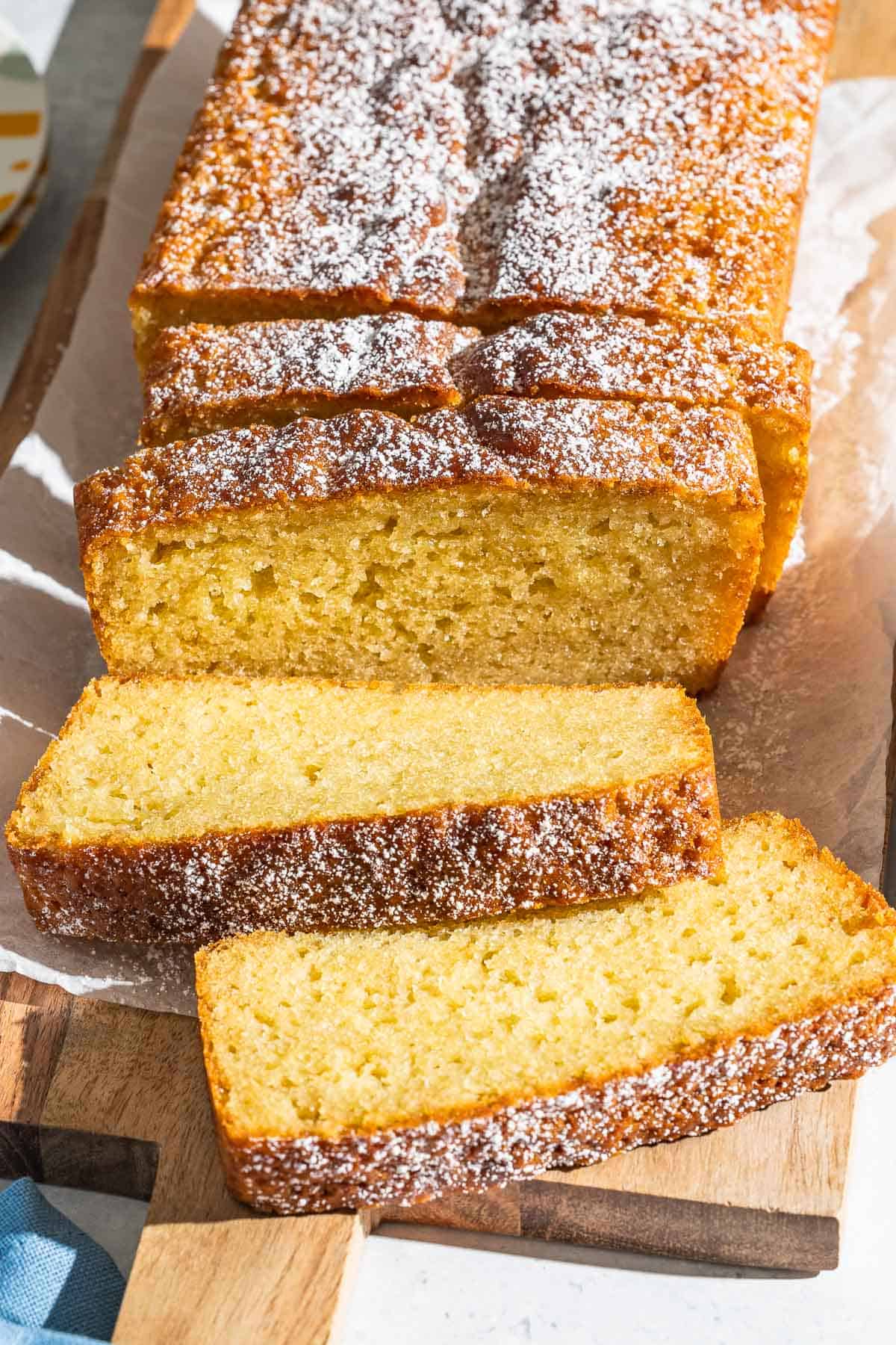 A close up of yogurt cake cut into slices on a parchment lined cutting board.