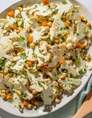 An overhead photo of a shaved cauliflower salad in a serving bowl. Next to this is a set of wooden serving utensils on a cloth napkin.