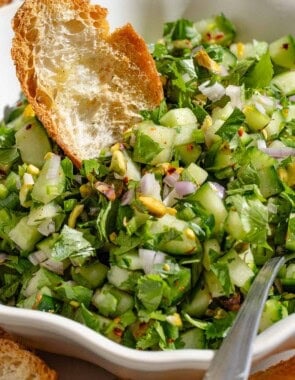 A close up of a bowl of cucumber salsa with a toasted baguette slice and a spoon.