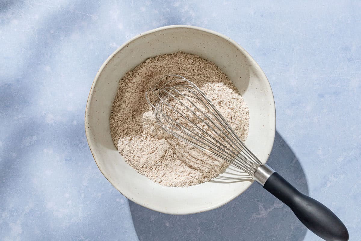 An overhead photo of the dry ingredients for the whole wheat fig bread in a bowl with a whisk.