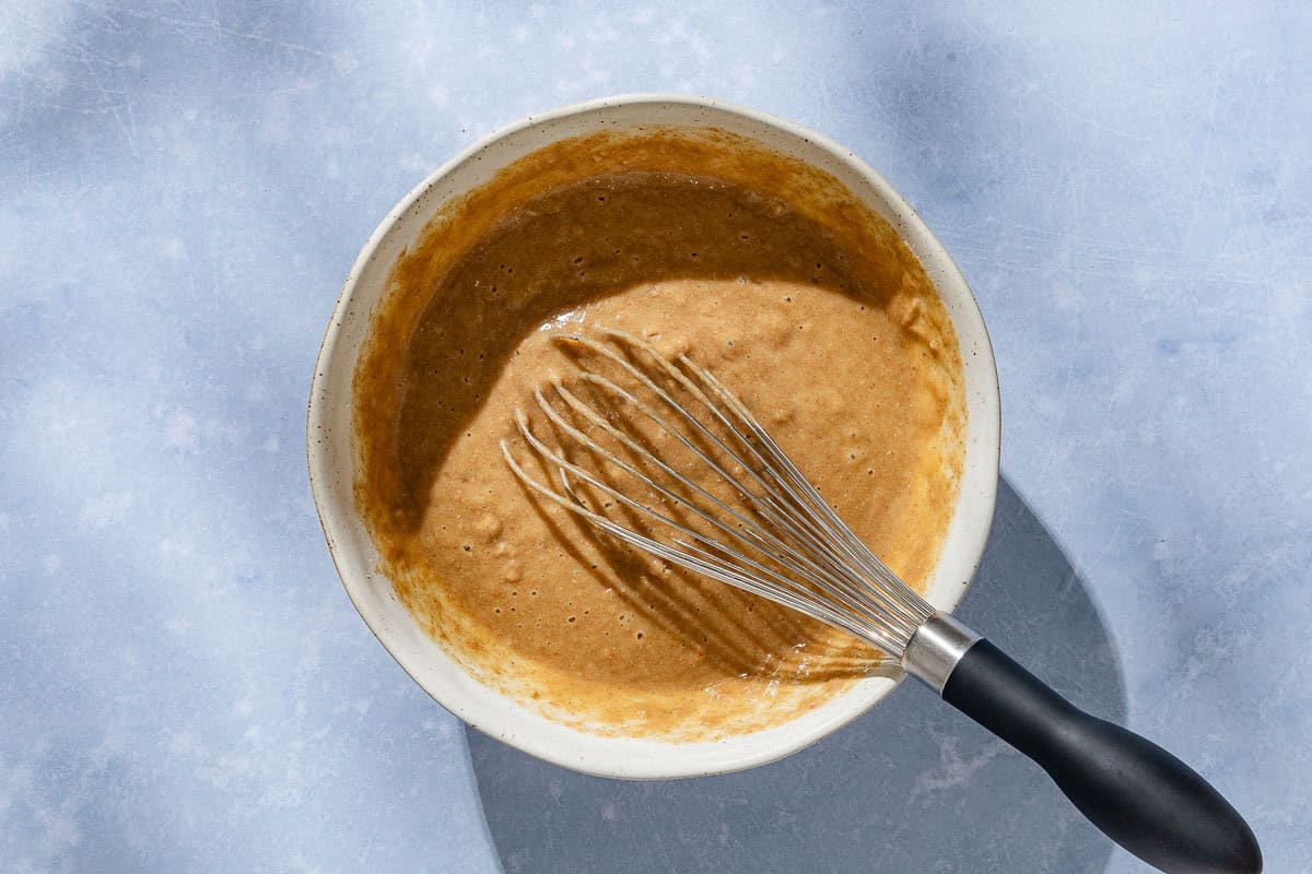 An overhead photo of the batter for the whole wheat fig bread in a bowl with a whisk.