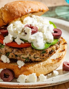 A close up of a greek style lamb burger on a plate.