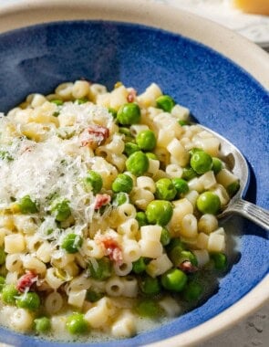 A close up of pasta with peas in a bowl with a spoon.