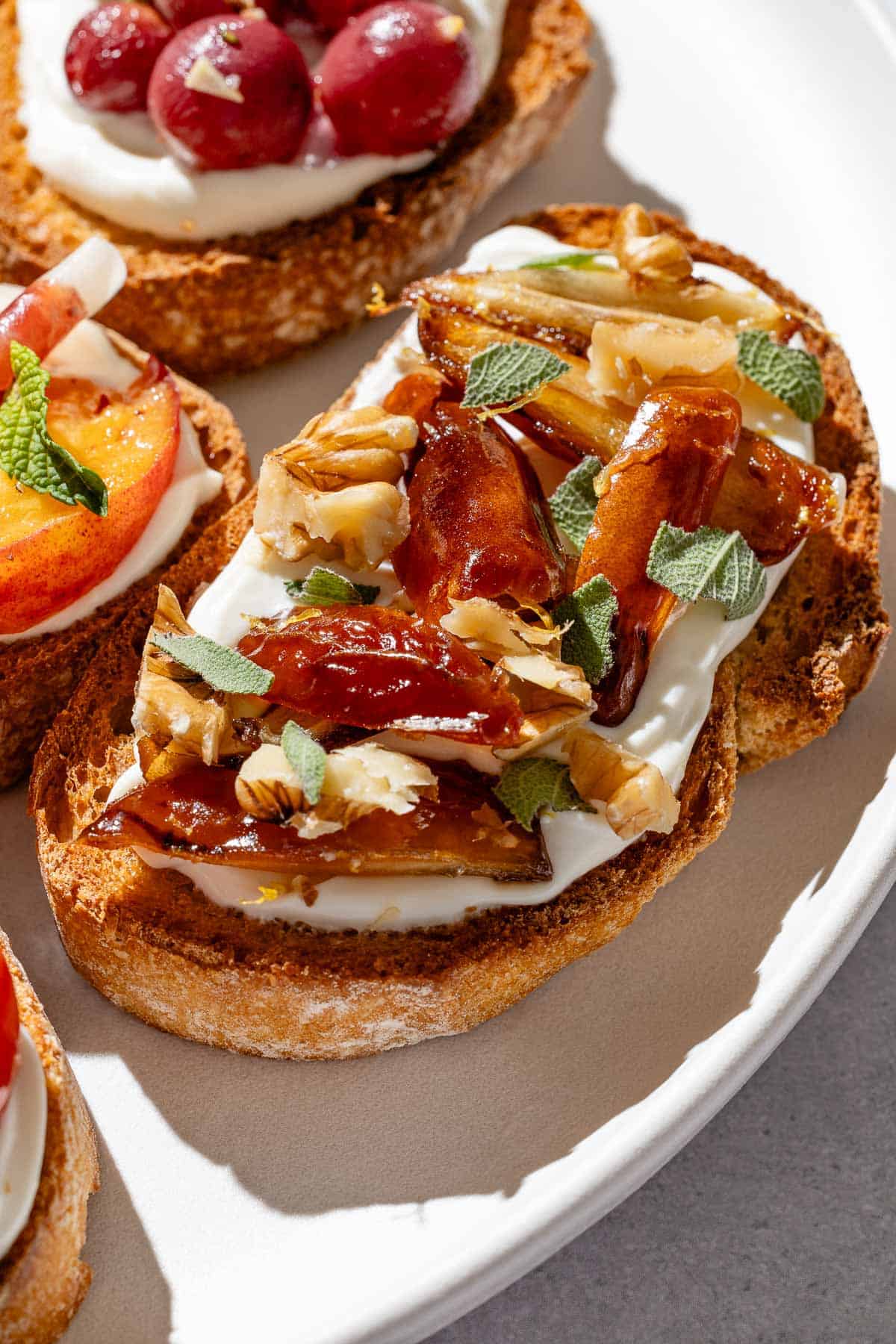 A close up of a warm date, walnut and sage ricotta toast on a serving platter.