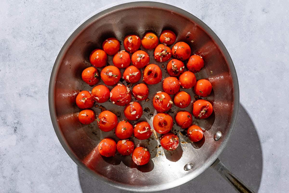 Cherry tomatoes being sauteed with salt, garlic and thyme in a skillet.