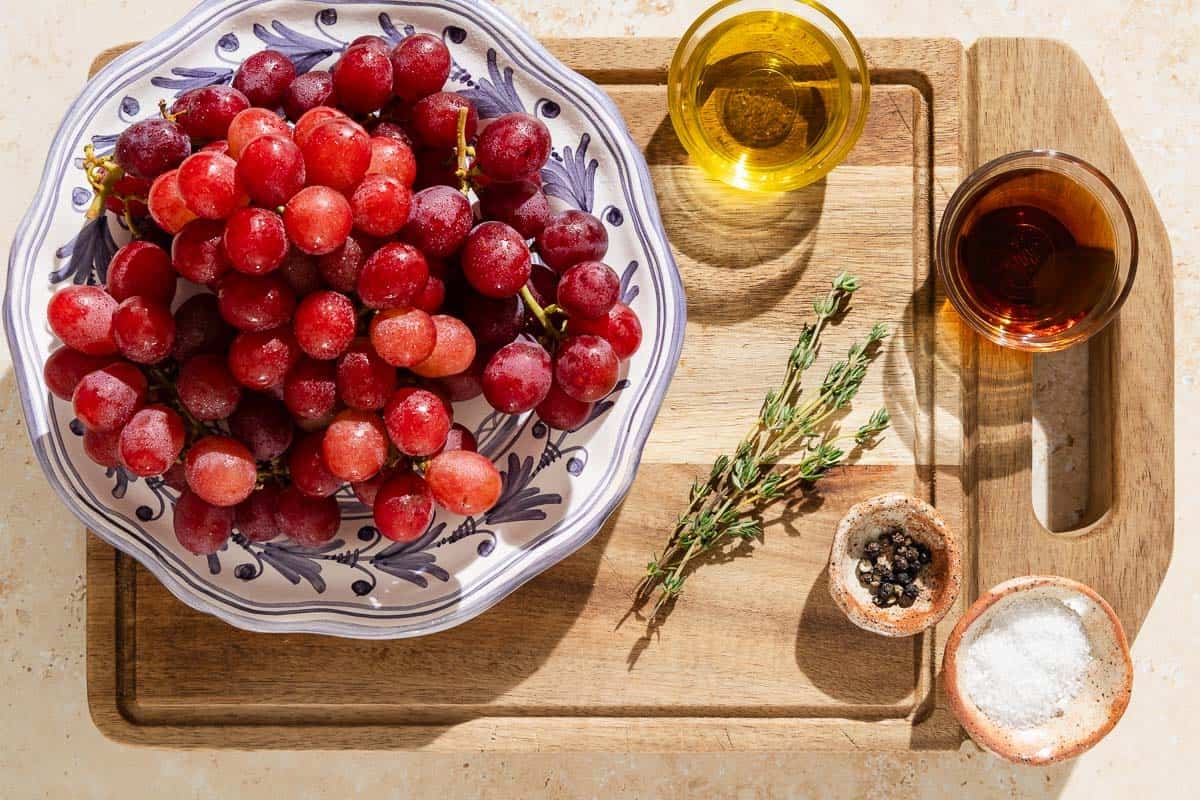 Ingredients for roasted grapes including grapes, olive oil, sherry vinegar, salt, black pepper and fresh thyme.