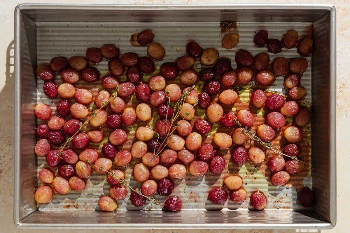 An overhead photo of roasted grapes with sherry and thyme in a baking pan.