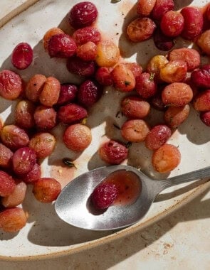 An overhead photo of roasted grapes with sherry and thyme on a plate with a spoon.