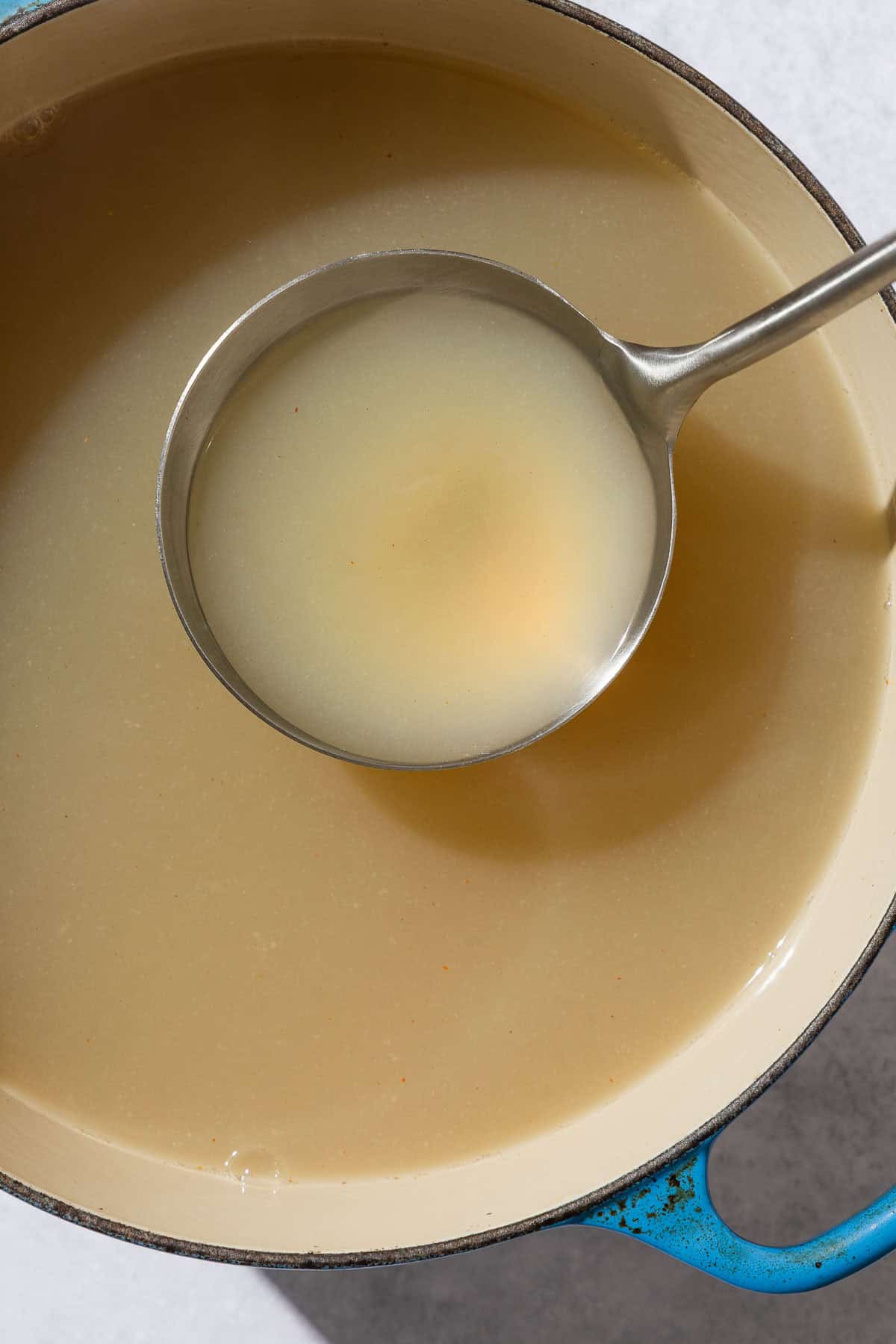 An overhead photo of seafood stock in a ladle being held over a pot of the stock.