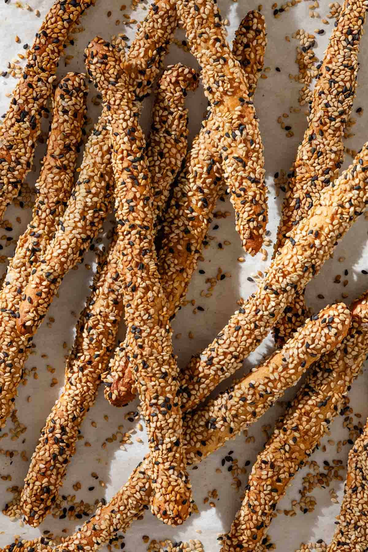 A close up of baked crispy sesame breadsticks on parchement.