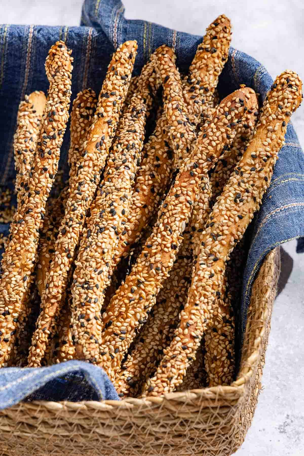 A close up of baked crispy sesame breadsticks in a basket lined with a cloth towel.