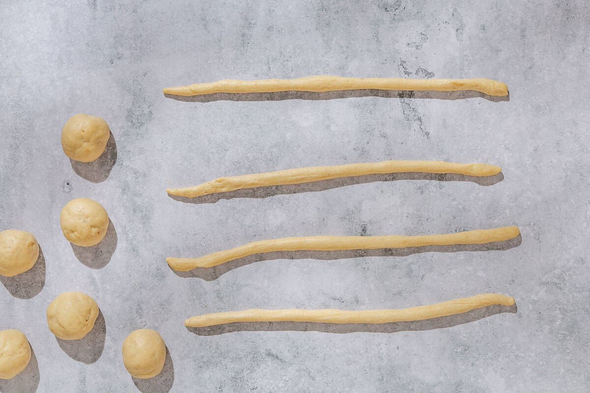 An overhead photo of 6 little balls of dough next to 4 ropes of dough.