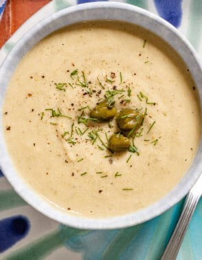 An overhead photo of a bowl of tonnato sauce topped with dill and capers on a plate with a spoon.