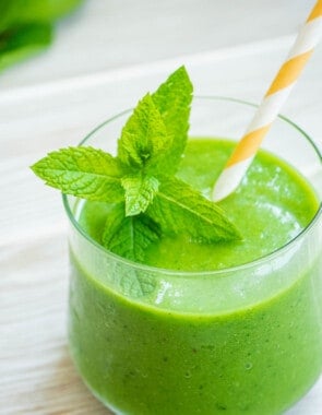 a vegan green smoothie in a glass with fresh mint and a yellow and white straw.