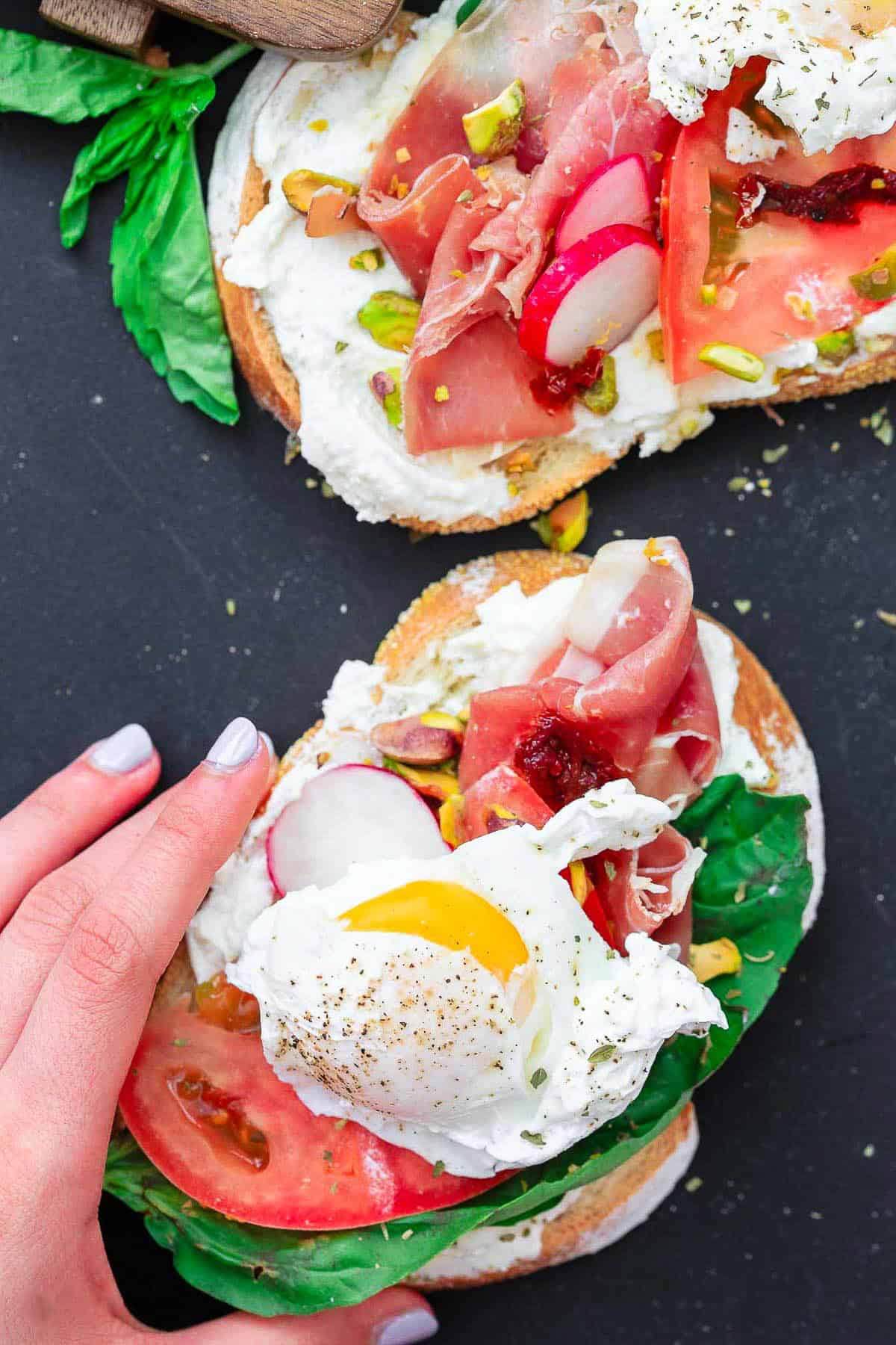 Suzy's hand about to pick up one open faced sandwich.