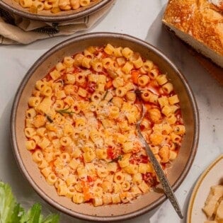 Overhead shot of a bowl of pasta e ceci with freshly grated parmesan cheese on top and parsley, parmesan, and bread on the side.